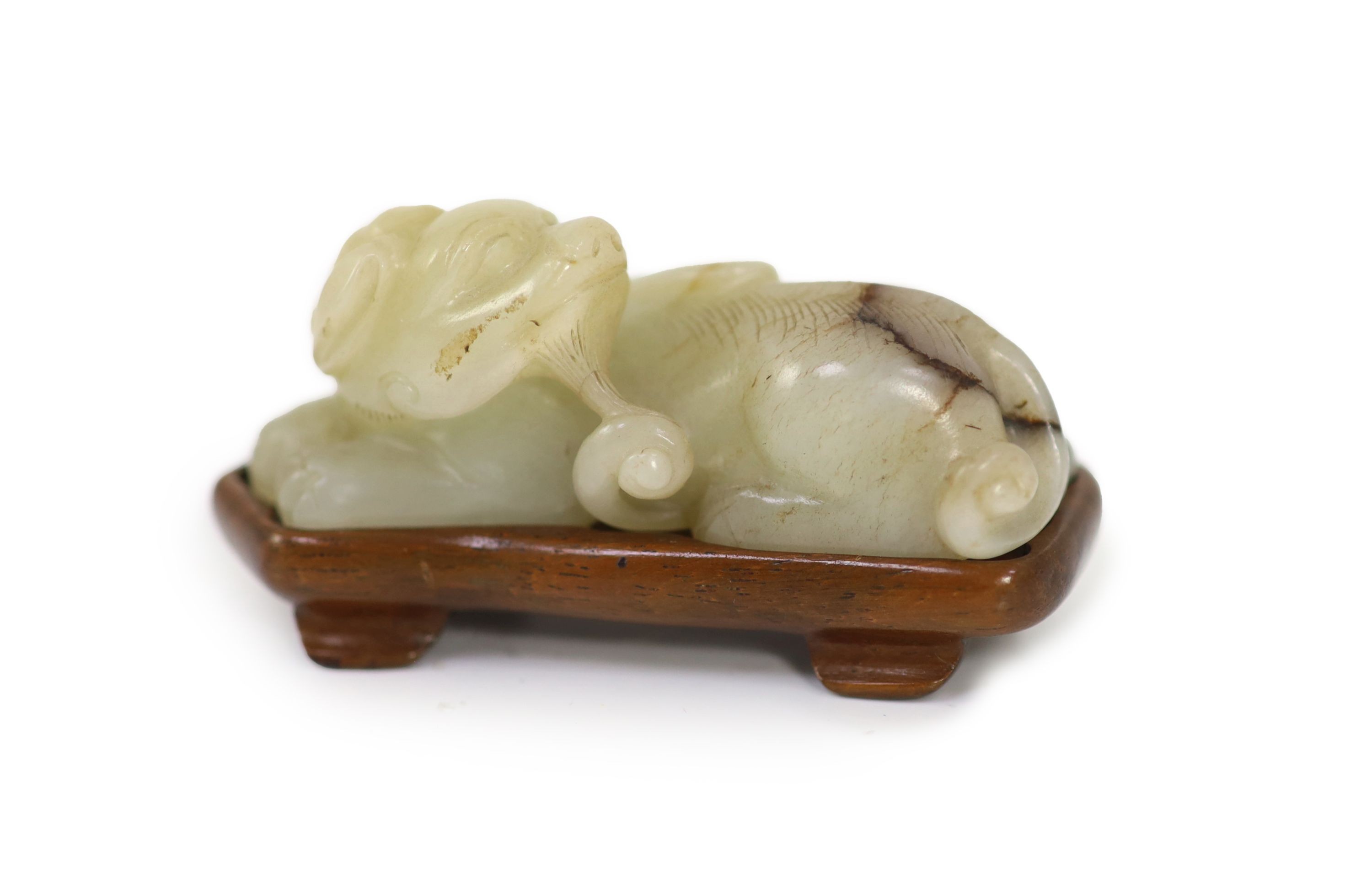 A Chinese pale celadon and brown jade figure of a lion-dog, 18th/19th century, 6.7cm long, wood stand